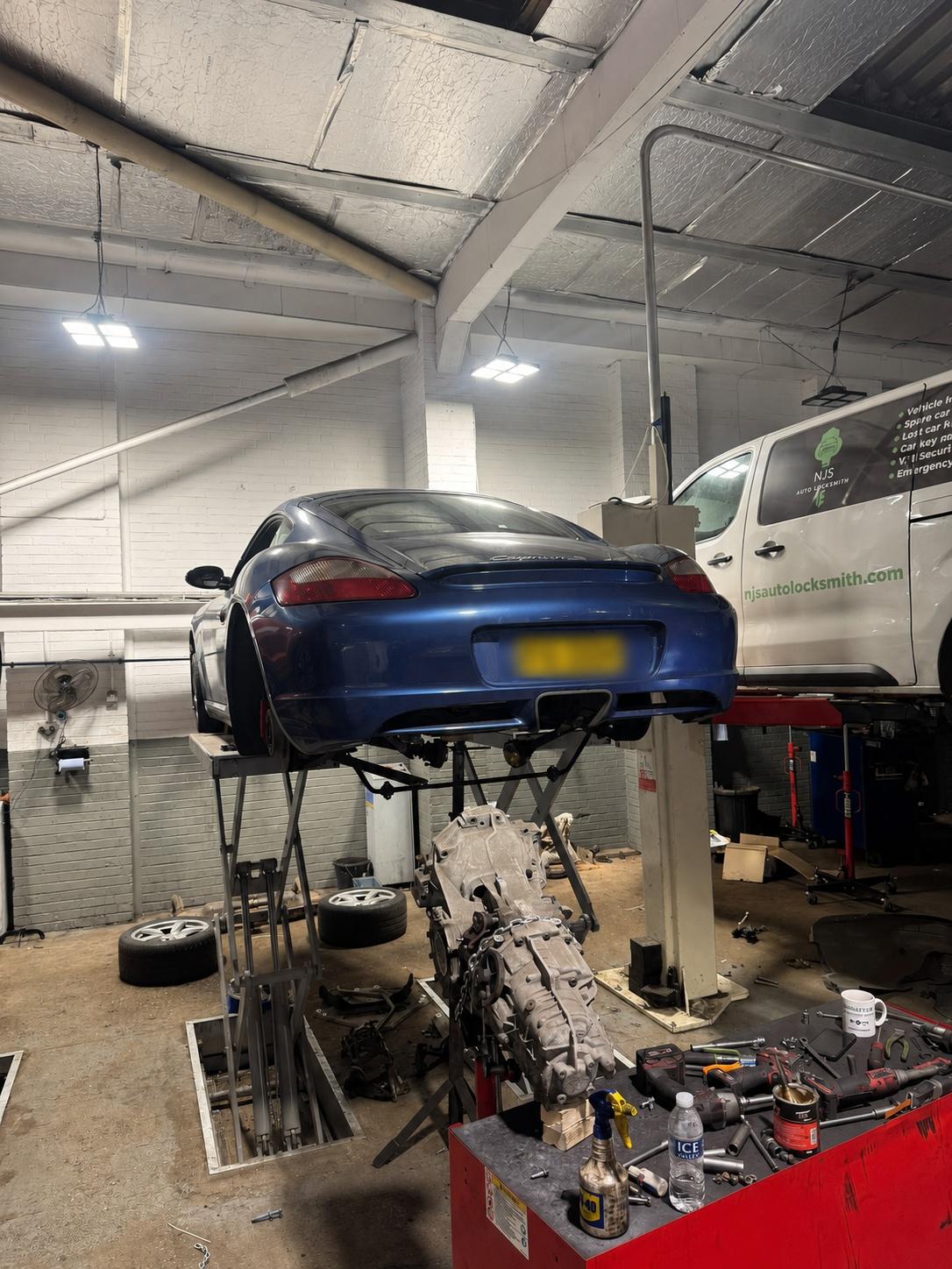 Dark blue sports car raised on a garage lift with a removed transmission below