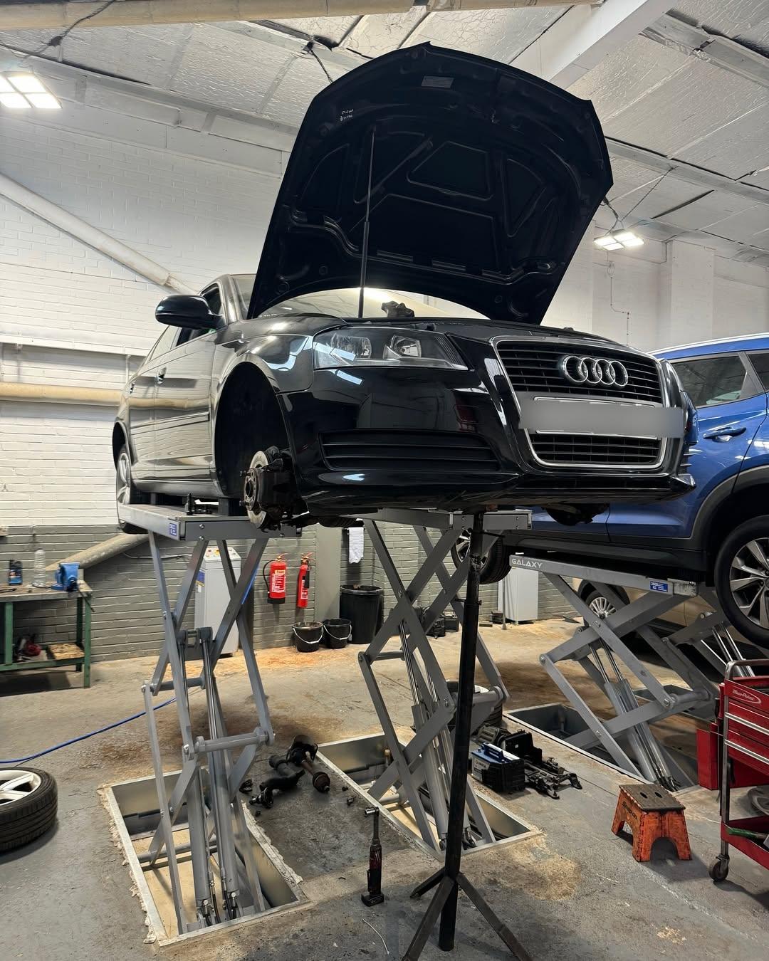 Black Audi raised on a garage lift with its bonnet open and front wheel removed